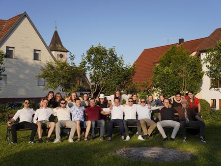 Eine Gruppe von jungen Erwachsenen sitzt gut gelaunt, teilweise mit Sonnenbrille in l&auml;ssiger Atmosph&auml;re auf einer Bank!